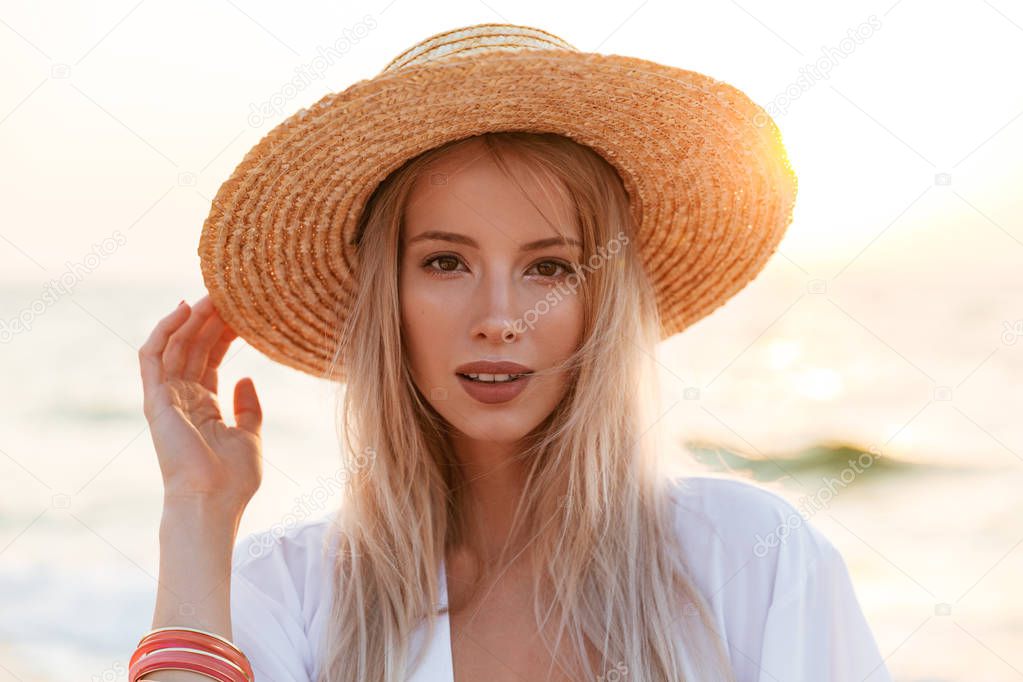 Image of beautiful cute blonde woman wearing hat outdoors at the beach looking camera.