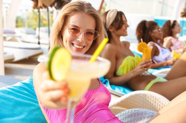 Dört genç kadınları birlikte rahatlatıcı bir yüzme havuzu Resort'ta, kokteyl içme, cam gösterilen mayolar