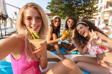 Genç mutlu duygusal grup swimwears içinde giyinmiş havuzu açık havada oturan kadın arkadaşıyla resmini çekmek bir selfie kamera tarafından.