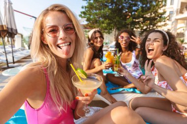 Genç mutlu duygusal grup swimwears içinde giyinmiş havuzu açık havada oturan kadın arkadaşıyla resmini çekmek bir selfie kamera tarafından.