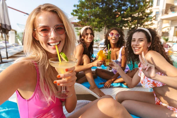 Mutlu duygusal grup havuzda açık havada oturup kokteyl içme kadın arkadaşıyla swimwears içinde giyinmiş genç görüntüsünü almak bir selfie kamera tarafından.