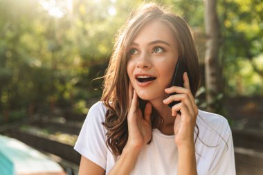 Genç kız üstünde hareket eden telefon vasıl belgili tanımlık park açık havada konuşurken gülümseyen