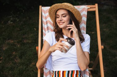 Genç kız üzerinde bir hamak Şehir Park açık havada yaz aylarında dinlenme cep telefonu üzerinde konuşurken paket servisi olan restoran kahve içiyorsun gülümseyen