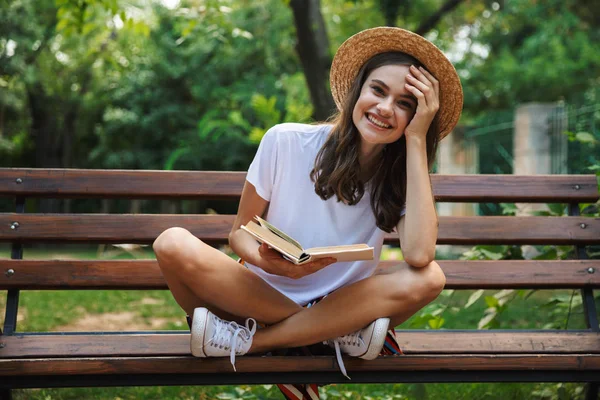 Εύθυμη Νεαρή Κοπέλα Διαβάζοντας Ένα Βιβλίο Ενώ Κάθεται Στο Πάρκο — Φωτογραφία Αρχείου