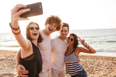 Sevgi dolu mutlu arkadaşlar grup fotoğrafı açık havada beach almak bir selfie tarafından cep telefonu barış hareketi ile çiftler.