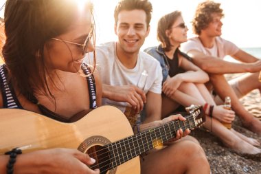 Grup mutlu genç arkadaşlar eğlenmeye zaman birlikte sahilde bira içme, kamp sırasında gitar çalmak,