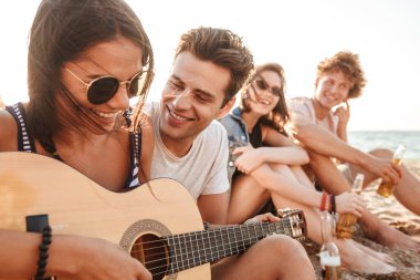 Mutlu arkadaş seven çift açık havada üzerinde oyun sırasında gitar üzerinde oturan plaj fotoğrafı.