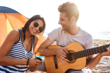 Sevimli arkadaşlar açık havada üzerinde oyun sırasında gitar üzerinde oturan plaj seven çift görüntü.