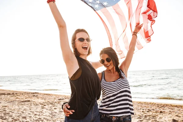 在海滩上快乐的女性朋友举着美国国旗玩乐的照片 — 图库照片