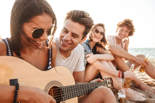 屋外でギターをプレイしながら座っているビーチのカップルを愛する幸せな友人の写真 — ストック写真