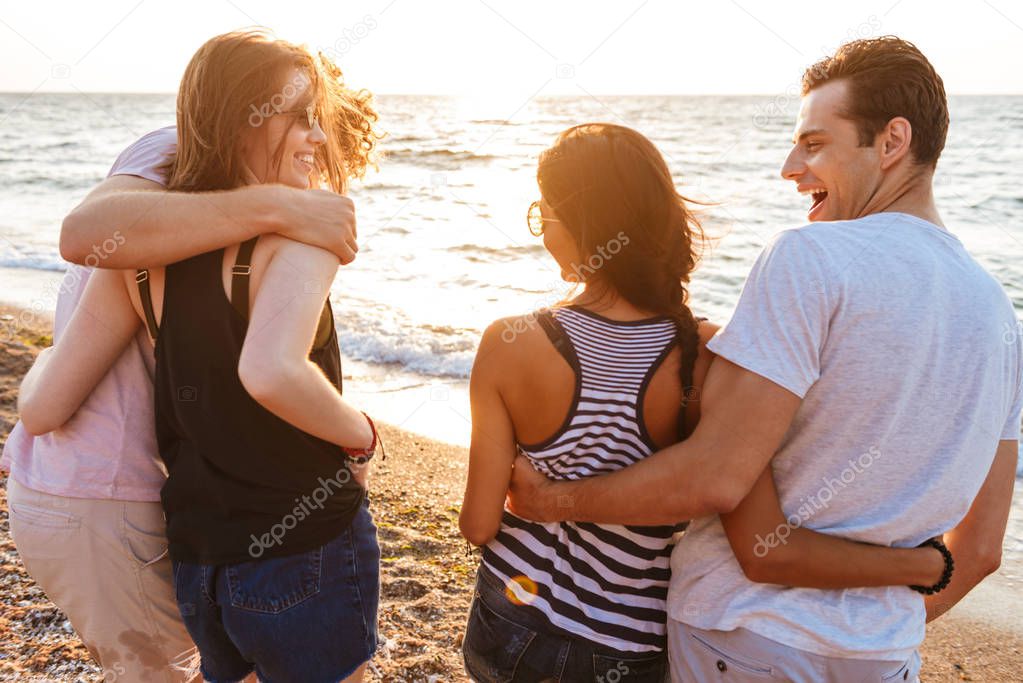 Image of excited group of friends loving couples walking outdoors on the beach having fun.
