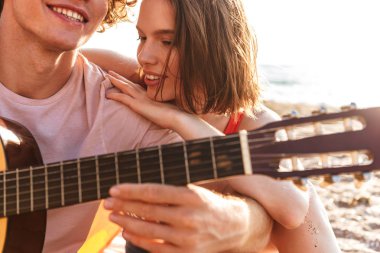 Mutlu genç çiftin birlikte kumsalda kamp, gitar çalmak, dinlenme resim kırpılmış