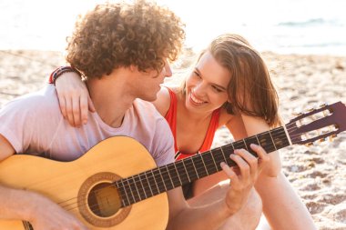 Güzel genç çift birlikte kumsalda kamp, gitar çalmak, dinlenme