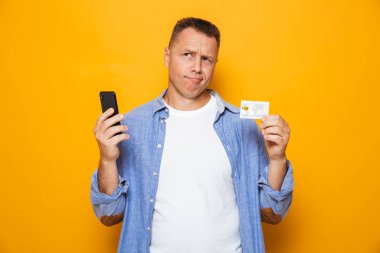Kredi kartı üzerinde sarı arka plan izole tutan adam cep telefonuyla portresi karışık bir orta yaşlı