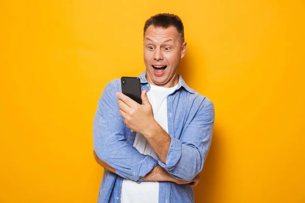 Heyecanlı Bir Orta Yaşlı Adam Cep Telefonu Üzerinde Sarı Arka — Stok fotoğraf