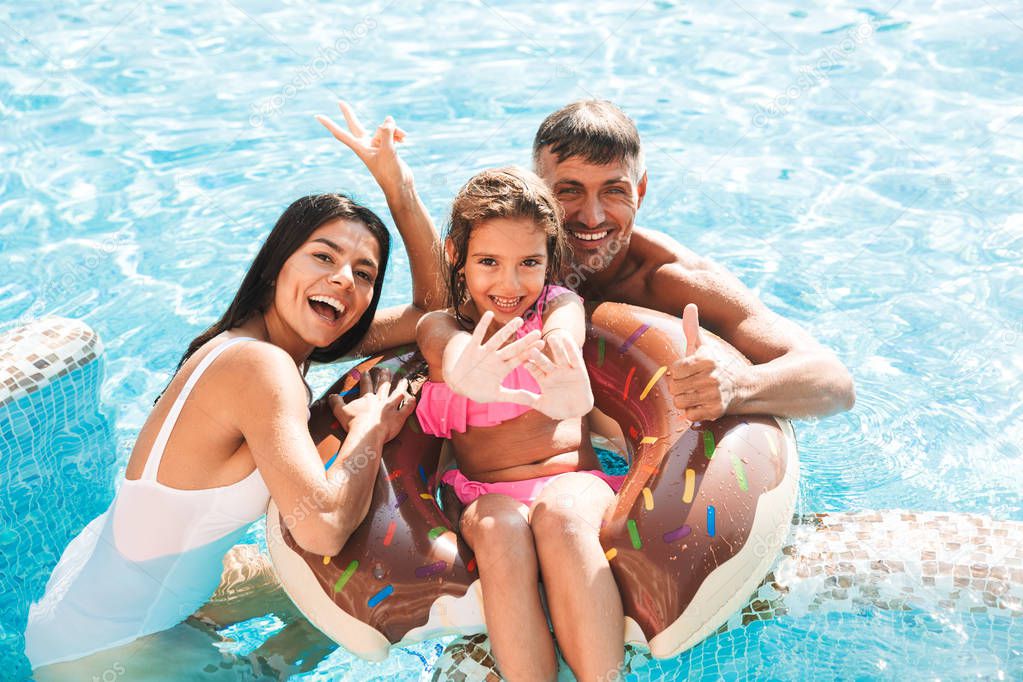Excited young family having fun together at the swimming pool outdoors in summer, swimming with inflatable ring donut