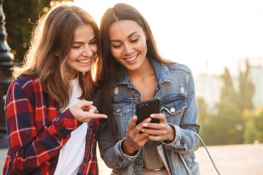 Genç kadın arkadaş öğrencilerin cep telefonuyla Park'ta yürüyordunuz şaşırtıcı görüntü.