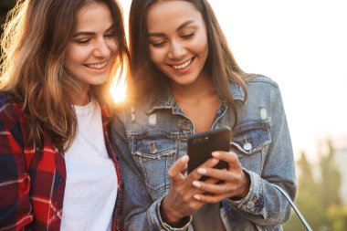 Genç kadın arkadaş öğrencilerin cep telefonuyla Park'ta yürüyordunuz şaşırtıcı görüntü.