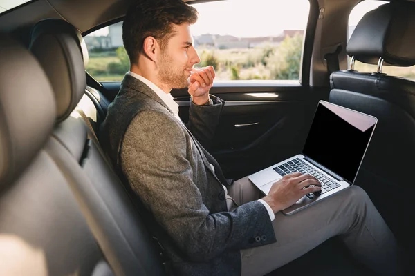ビジネス クラス車に座ってしばらくラップトップに取り組んでのスーツでハンサムな男の肖像 — ストック写真