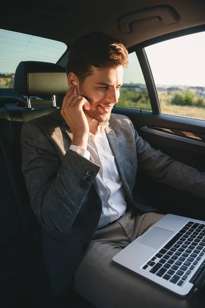 成功男子穿着西装和耳塞工作在笔记本电脑 而回到坐在商务舱车的照片 — 图库照片