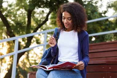 Ödev yapmak bir gülümseyen genç Afrikalı kız parkta, dinlenme sırt çantası ile portresi