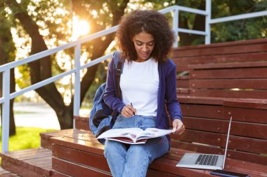 Dergi okuma çok hoş bir genç Afrikalı kız parkta, dinlenme sırt çantası ile portresi