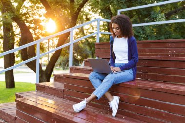 Açık havada park dizüstü bilgisayar kullanan basamaklarında oturan mutlu Afrika genç kadın görüntüsünü.