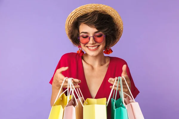 買い物中毒女性 代購入紫色の背景を分離するとカラフルな紙のショッピング バッグを保持している麦わら帽子の写真 — ストック写真