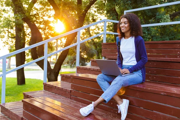 快乐的非洲年轻妇女的形象坐在户外公园上的步骤使用膝上型计算机 — 图库照片