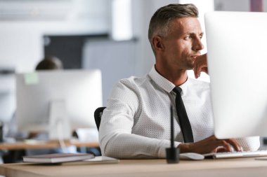 Yetişkin iş adamı 30'lu giyen beyaz gömlek ve kravat ofiste bilgisayar başına oturmuş görüntü