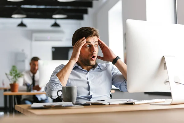 Confundido Gerente Masculino Conmocionado Usando Computadora Sosteniendo Cabeza Mientras Está —  Fotos de Stock