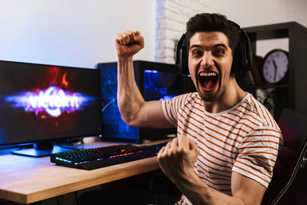 Portrait of caucasian gamer guy screaming and rejoicing while playing video games on computer wearing headphones
