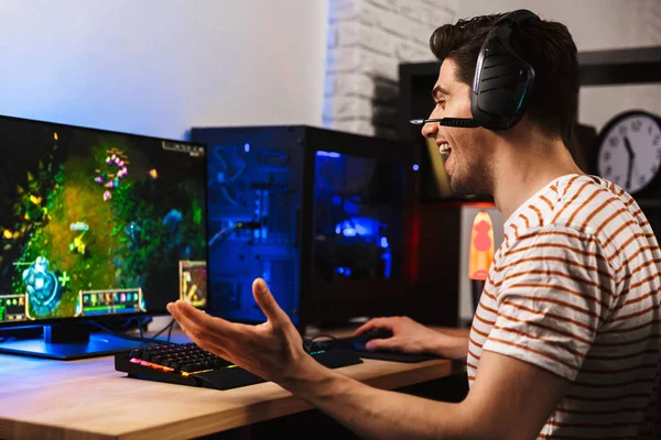 ヘッドフォンを身に着けている カラフルなキーボードのバックライトを使用して コンピューターでビデオ ゲームをプレイ陽気なゲーマー男のイメージ — ストック写真
