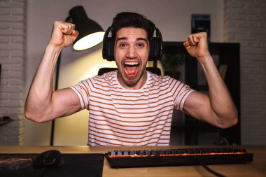 Çok mutlu mutlu genç adam 20'li yaşlarda giyen kulaklık odasındaki masada oturan, video oyunları oynayan bağırarak portresi