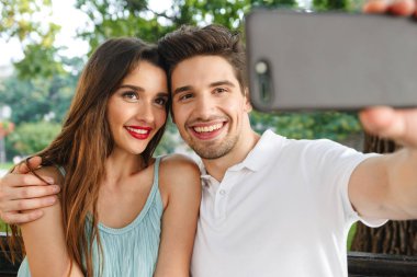 Genç tatlı sevgi dolu çift açık havada yapmak selfie cep telefonuyla oturan fotoğraf.