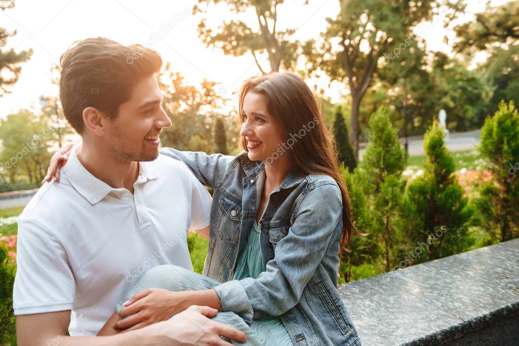 Image of happy young loving couple walking outdoors while hugging talking with each other.