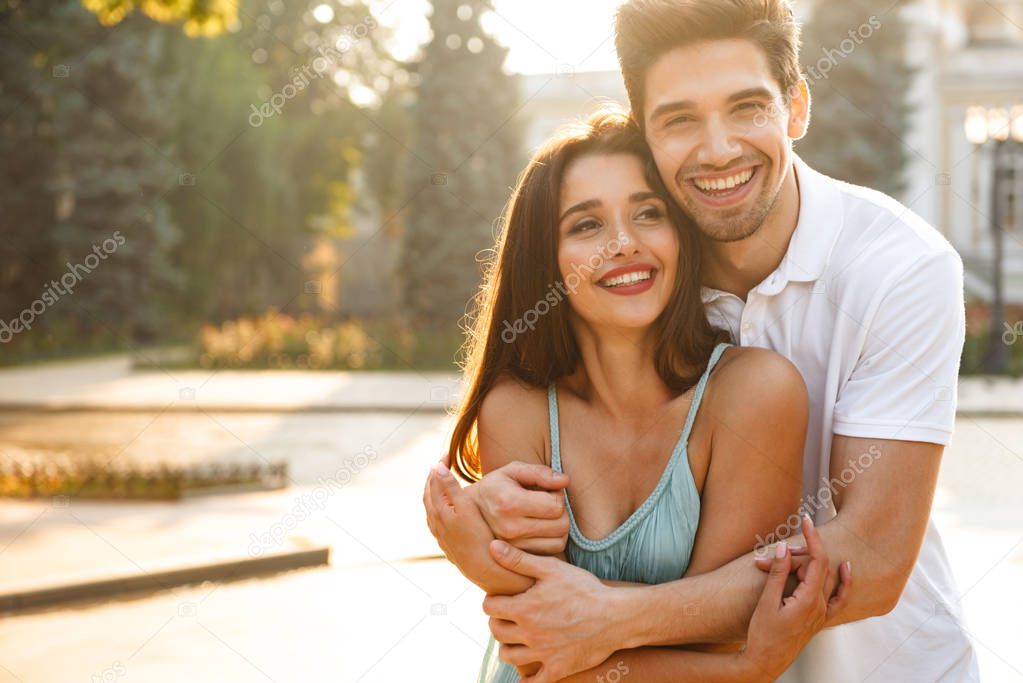 Image of happy young loving couple walking outdoors while hugging.