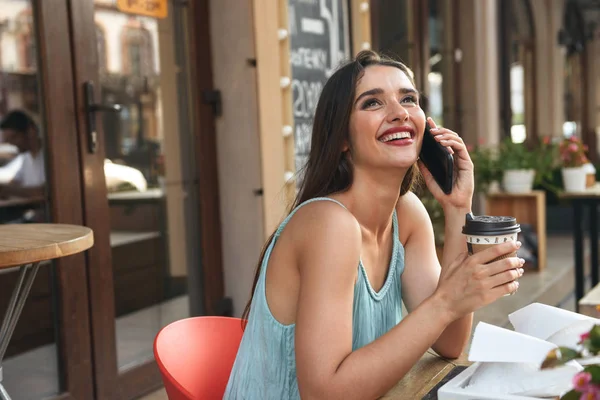 年轻快乐的女人坐在户外咖啡馆的形象 而手机喝咖啡交谈 — 图库照片