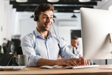 Fotoğraf çağrı merkezi bilgisayar tarafından oturan kulaklık ve mutlu operatör adam 20'li yaşlarda giyen ofis kıyafet