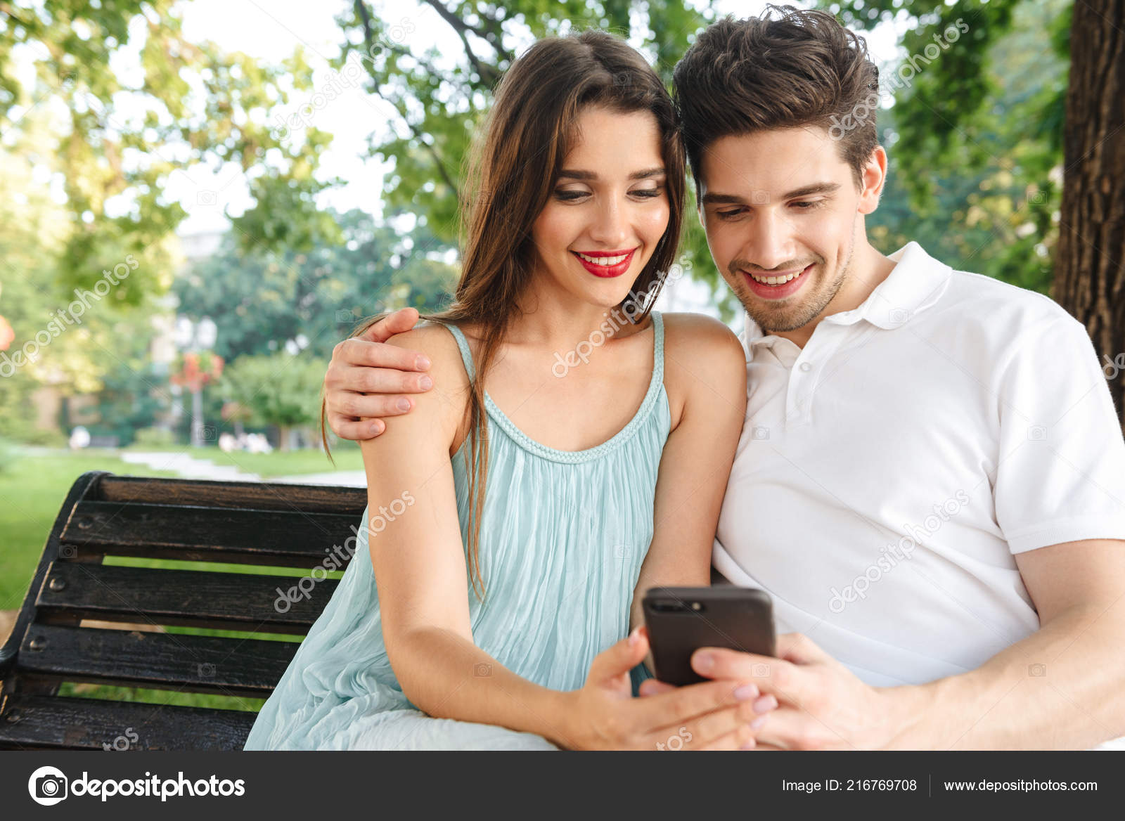 Photo Young Cute Loving Couple Sitting Outdoors While Using Mobile