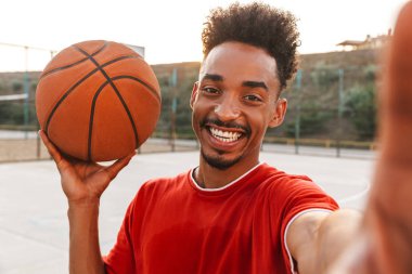 Afrika kökenli Amerikalı adam holding topu ve alma selfie basketbol parkta açık oynarken gülümseyen portresi