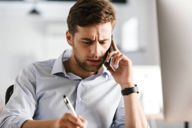 Smartphone ile konuşmak ve ofiste tabloda tarafından otururken bir şey yazma ciddi iş adamı