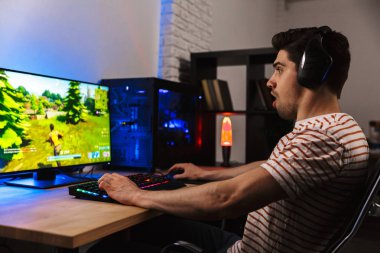 Arkadan aydınlatmalı renkli klavye kullanarak bilgisayarda video oyunları oynamak kulaklık heyecanlı adam görüntüsünü