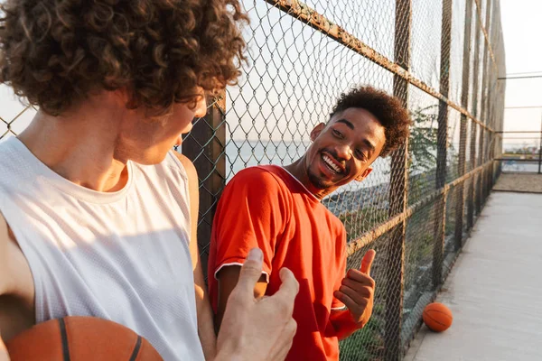 Двое Молодых Улыбающихся Мультиэтнических Баскетболистов Стоящих Спортивной Площадке Разговаривают — стоковое фото