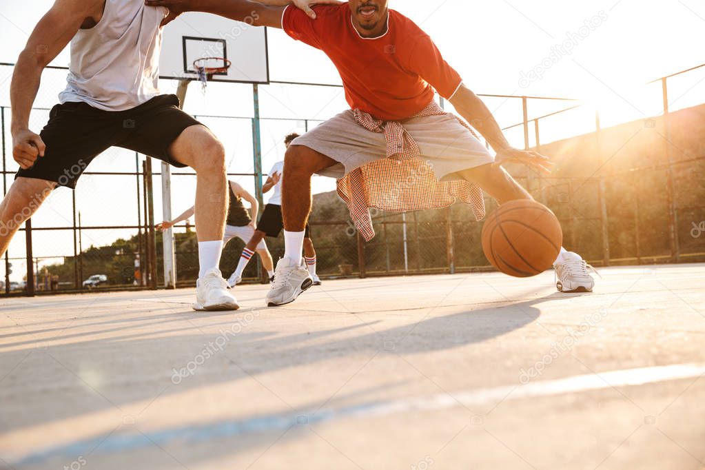 Cropped image of young multiethnic men basketball players playing basketball at the sport ground