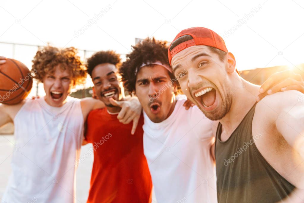 Photo closeup of young sporty men smiling and taking selfie while playing basketball at playground outdoor during summer sunny day