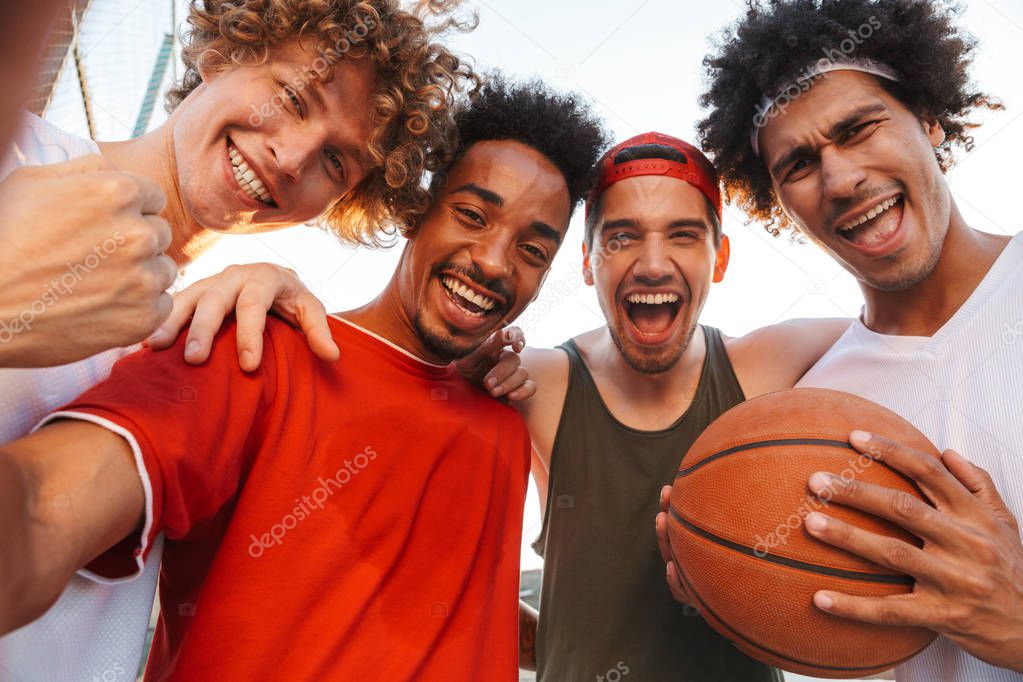 Photo closeup of handsome players men smiling and taking selfie while playing basketball at playground outdoor during summer sunny day