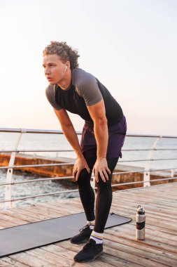 Kulaklık ile müzik dinlemek egzersiz yaptıktan sonra kumsalda, dinlenme çok yorgun bir sporcu portresi