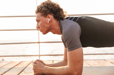 Kulaklık ile müzik dinlemek tahta egzersiz fitness mat plaja, güçlü bir sporcu portresi