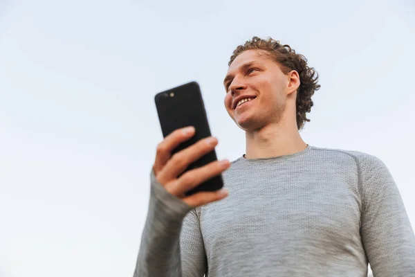 Vista Dal Basso Smiling Curly Sportsman Che Tiene Smartphone Distoglie — Foto Stock